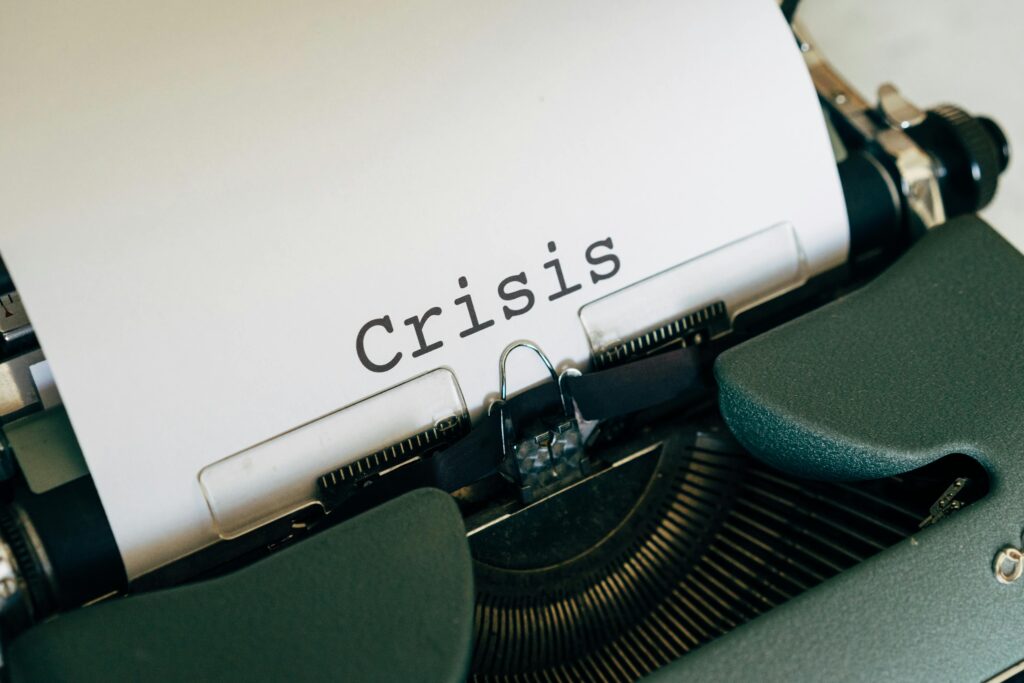 A close-up of a white paper inserted into the roller of a vintage typewriter, with the keys visible in the background, and a word "Crisis" was typed on it.