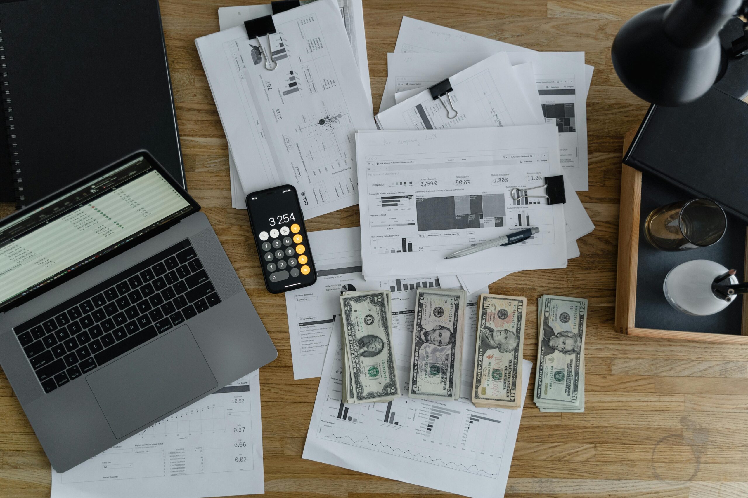 A flatlay photo showing financial statements, business plans, phone calculator and some cash.